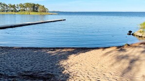 A beach with a wooden dock extending into calm waters, surrounded by trees and a clear sky. - 7 Person Holiday Home in Hagby (Ljungbyholm)