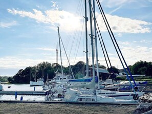 Un port de plaisance où sont amarrés de nombreux voiliers, entouré de verdure et sous un ciel dégagé.