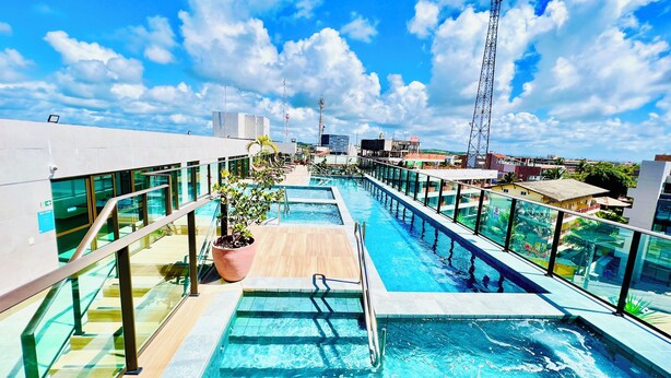 A rooftop pool with clear blue water, glass railings, and potted plants. - 1. Flat Premium Porto de Galinhas (Ipojuca)