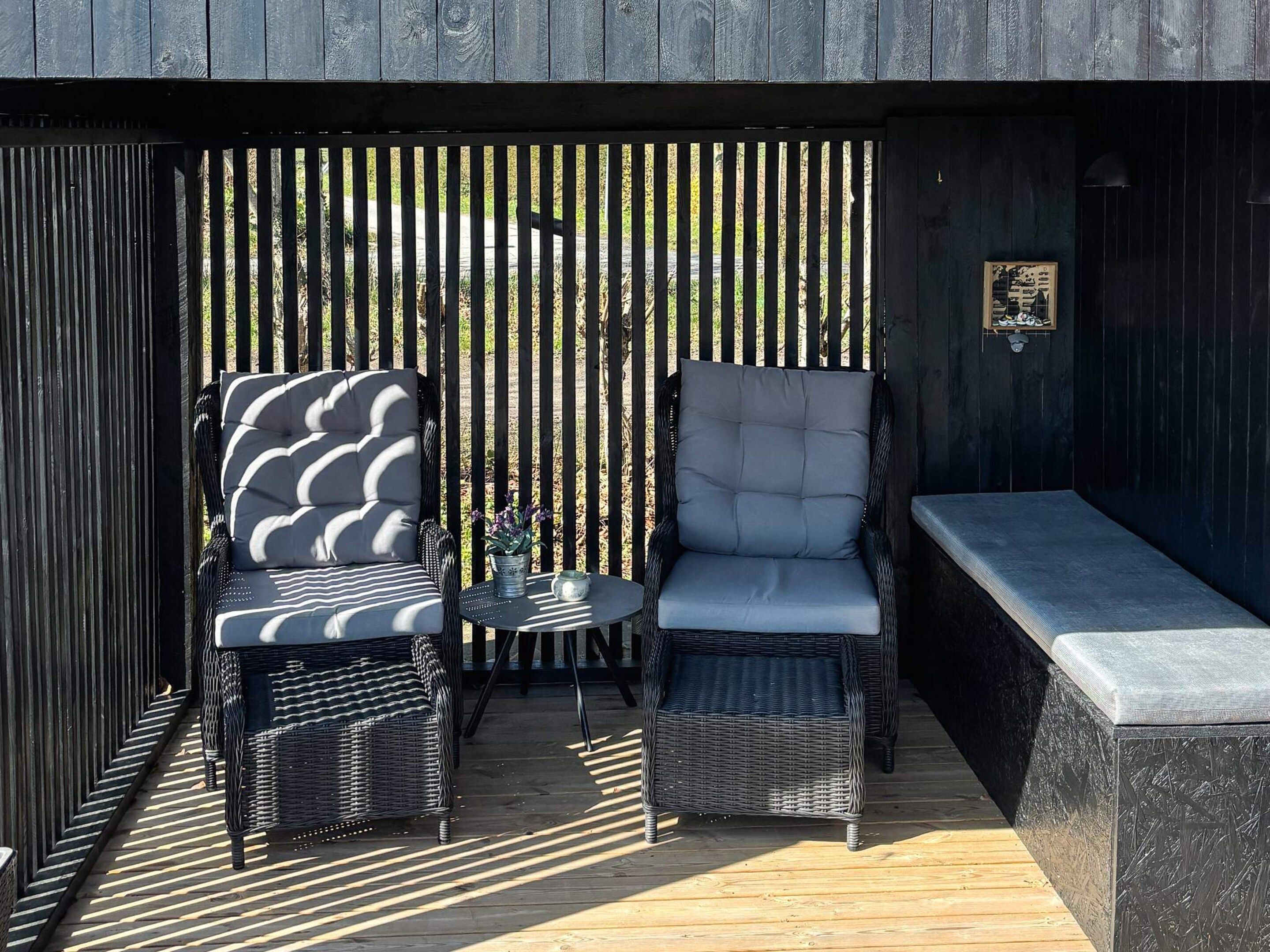 An outdoor seating area with wicker chairs and a bench, a small round table, and a decorative wall panel.