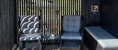 An outdoor seating area with wicker chairs and a bench, a small round table, and a decorative wall panel.