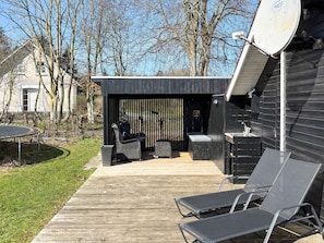 Une terrasse extérieure moderne avec une plateforme en bois, un espace salon couvert doté de meubles en osier et une antenne parabolique installée sur le bâtiment.
