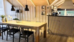 Uma mesa de jantar de madeira com cadeiras, luminárias pendentes e vista para o exterior.