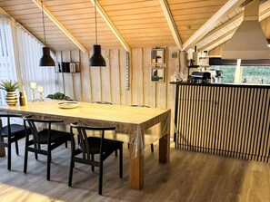 Uma mesa de jantar de madeira com cadeiras, luminárias pendentes e vista para o exterior.