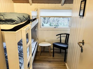Une petite pièce avec des lits superposés, une petite table, une chaise et une fenêtre donnant sur les arbres.