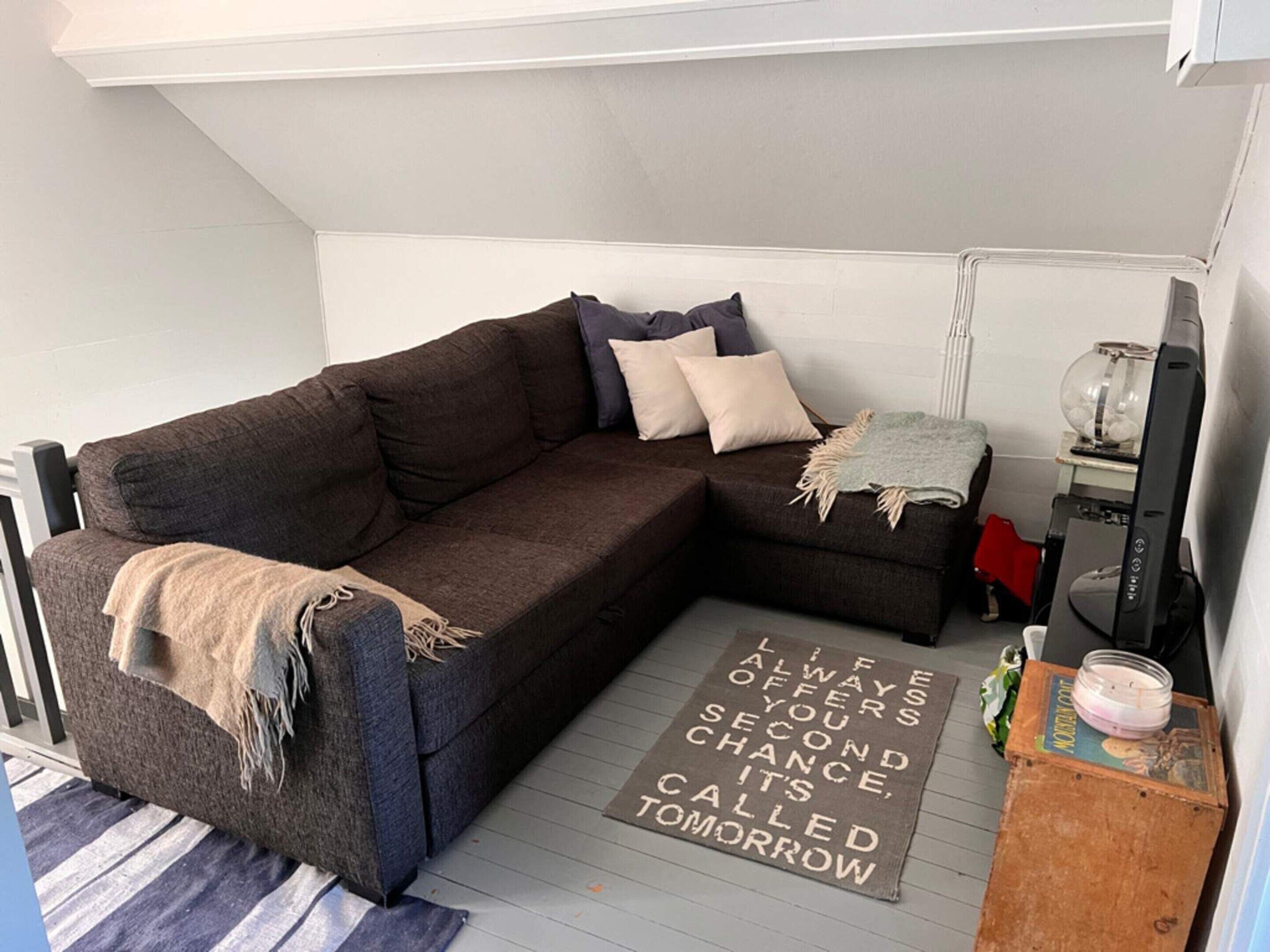 A cozy living room with a dark brown sectional sofa, a small side table, a television, and a motivational rug.