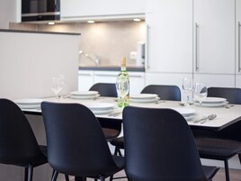 Et moderne spiseområde med et bord dækket til fire personer, stole og en flaske hvidvin.