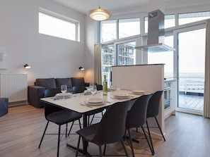 Un espace repas moderne avec une table dressée pour quatre personnes, un canapé et une vue sur l’extérieur.