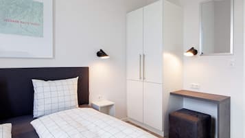 Ein Schlafzimmer mit Bett, Kleiderschrank, Nachttisch, Spiegel und Wandleuchte.