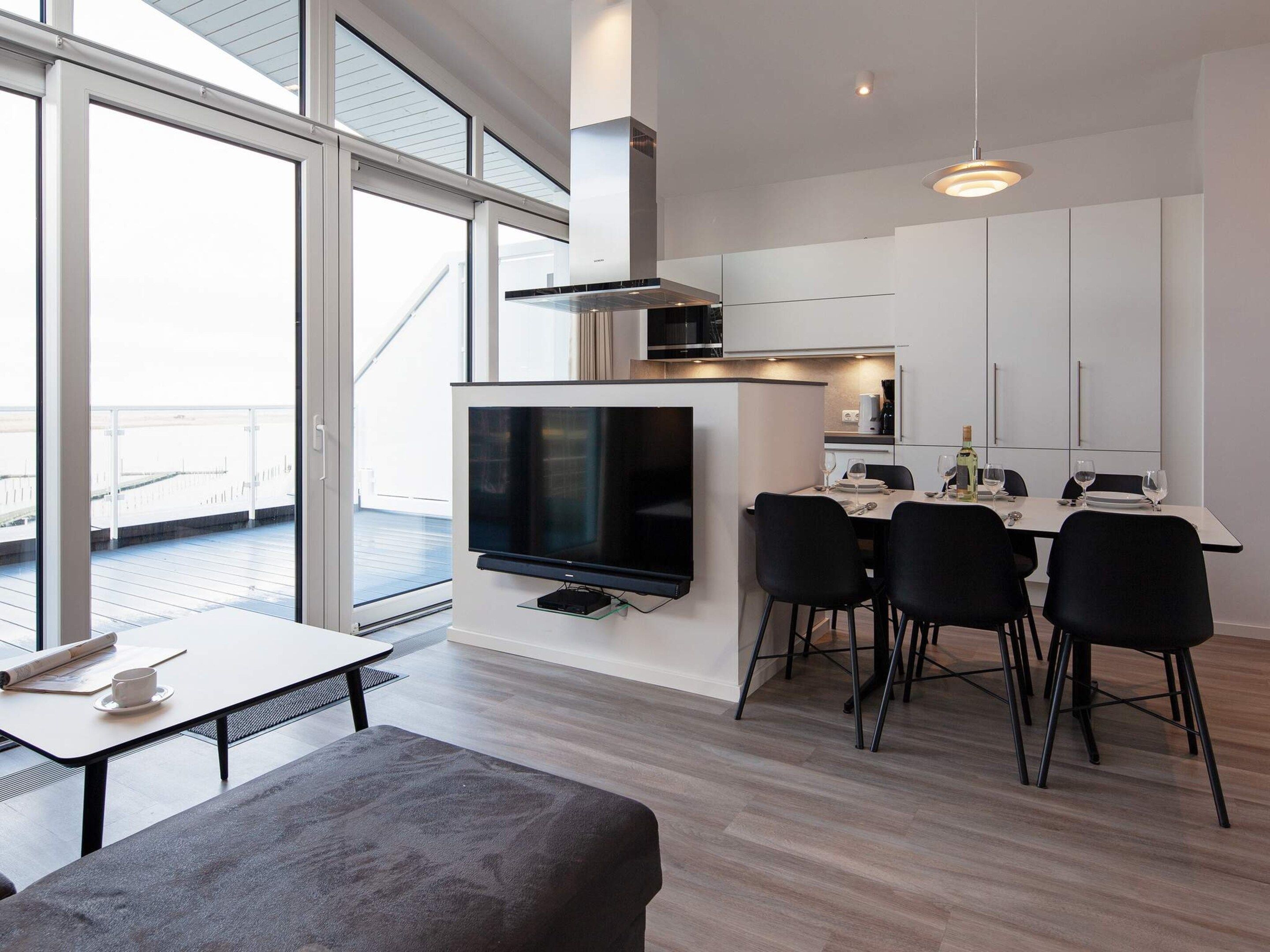 A modern kitchen with a flat-screen TV, dining area with chairs, and a balcony view.