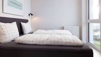 Ein modernes Schlafzimmer mit einem Bett, Kissen, einer Nachttischlampe und einem Fenster.