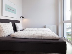 A modern bedroom with a bed, pillows, a bedside lamp, and a window.
