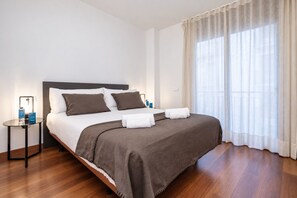 A hotel room with a bed, a bedside table, a lamp, and a window with curtains. - Sweett | Eixample 1D (Barcelona)