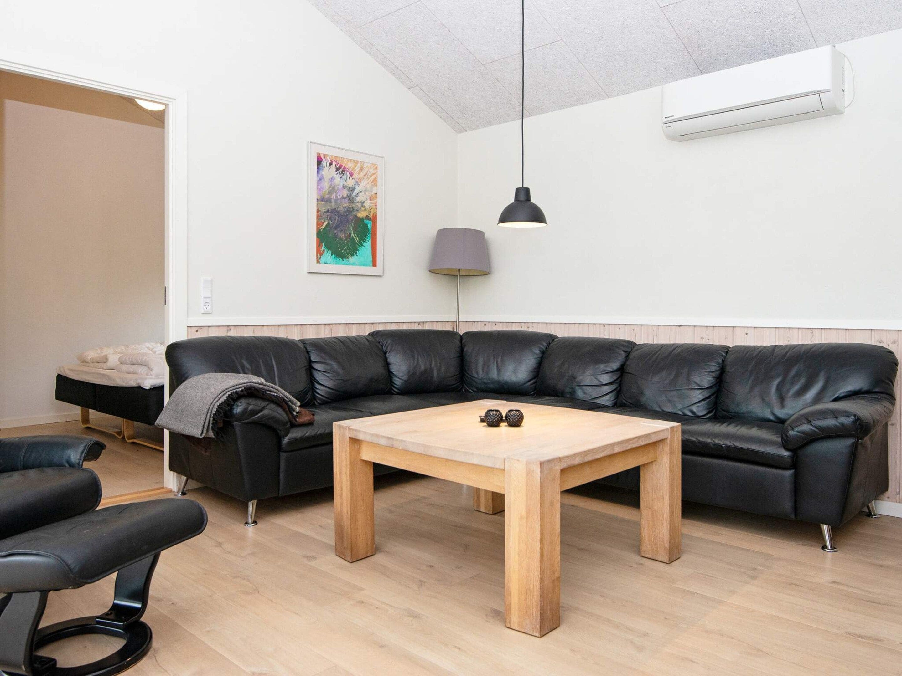 Una sala moderna con un sofá de cuero negro, una mesa de centro de madera y una silla negra.