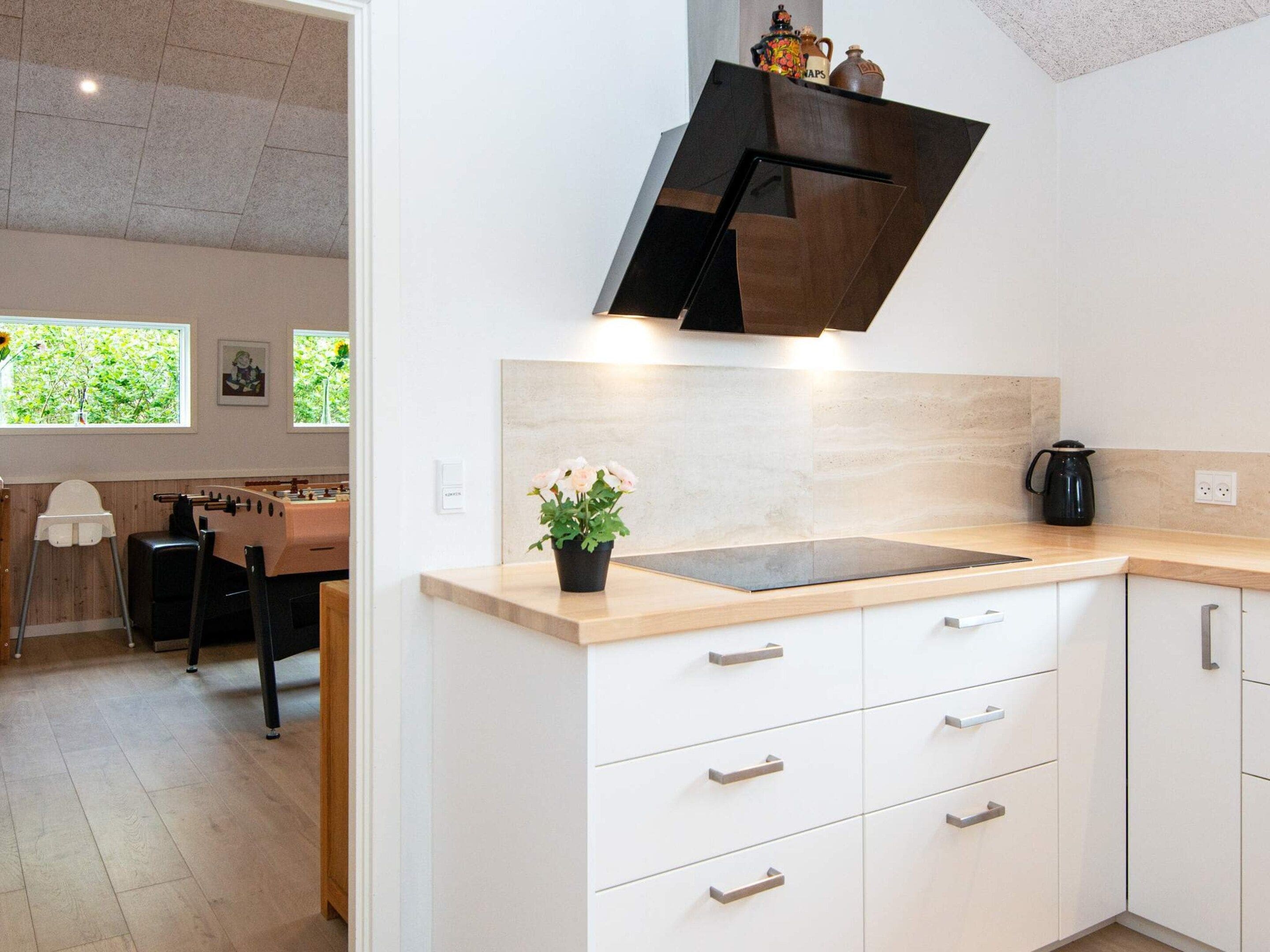 A modern kitchen with a wooden countertop, white cabinets, and a black range hood.