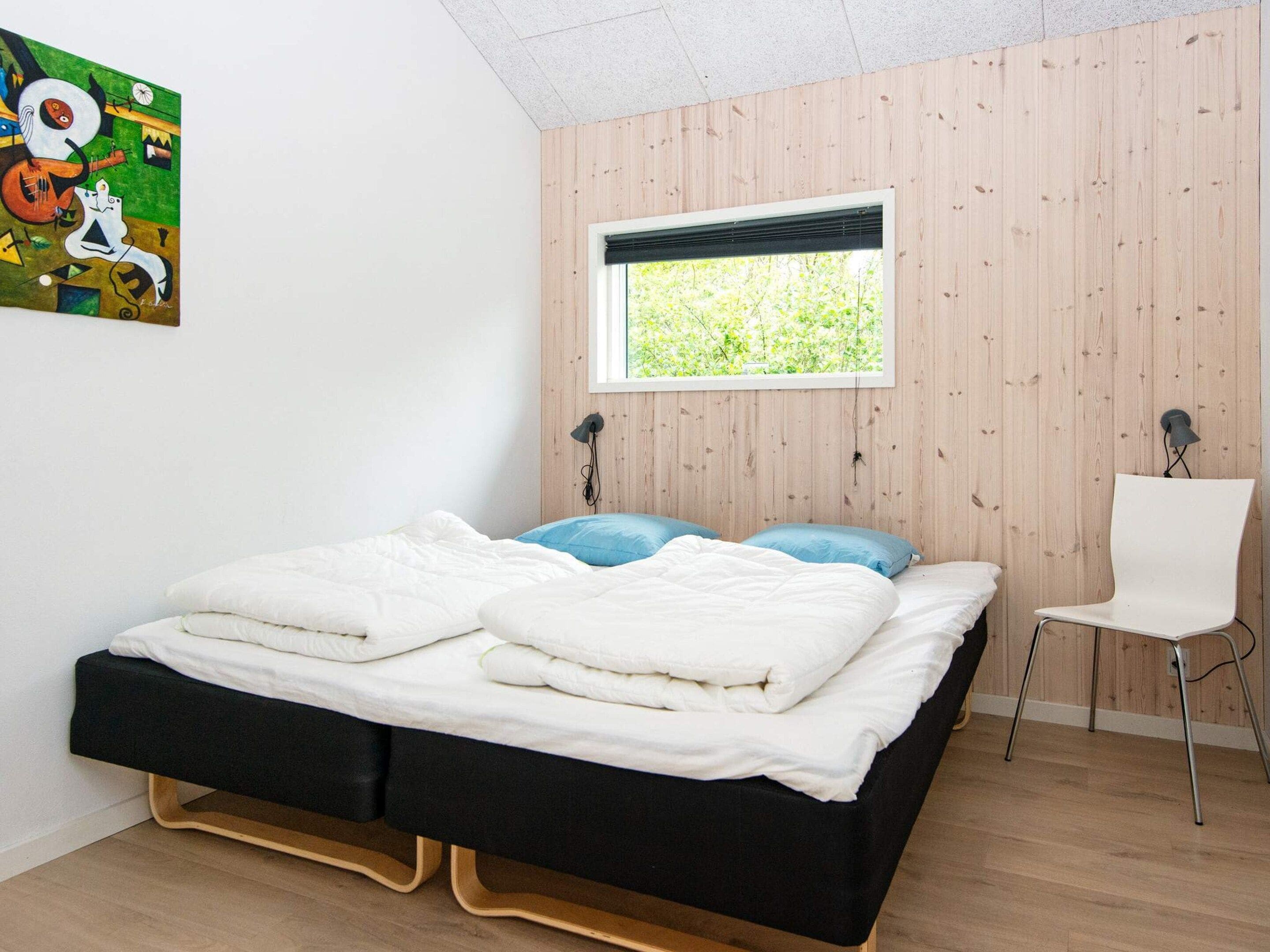 A bedroom with a bed, a window, a chair, and a painting on the wall.