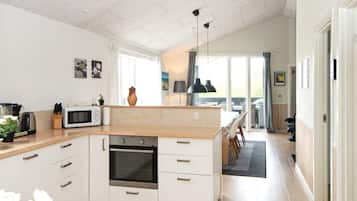 Cozinha moderna com ilha central, forno embutido e área de refeições com vista.