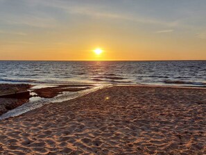En strand där solen går ner över havet och vågorna skvalpar försiktigt mot stranden.