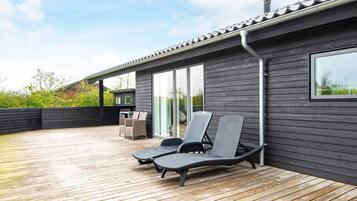 Una terraza moderna al aire libre con dos sillones, una mesa y una zona de barbacoa.