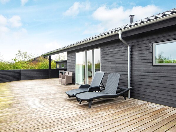 A modern outdoor deck with two lounge chairs, a table, and a grill area.