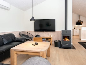 A modern living room with a black leather sofa, a wooden coffee table, a TV, and a wood-burning stove.