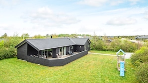 A modern house with a covered patio, a playhouse, and a grassy yard.