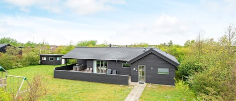 A modern two-story house with a covered patio, a small garden, and a gravel driveway.