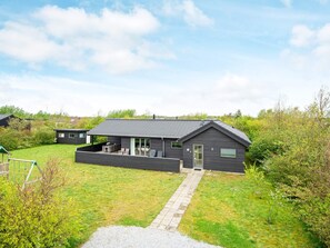 A modern two-story house with a covered patio, a small garden, and a gravel driveway.