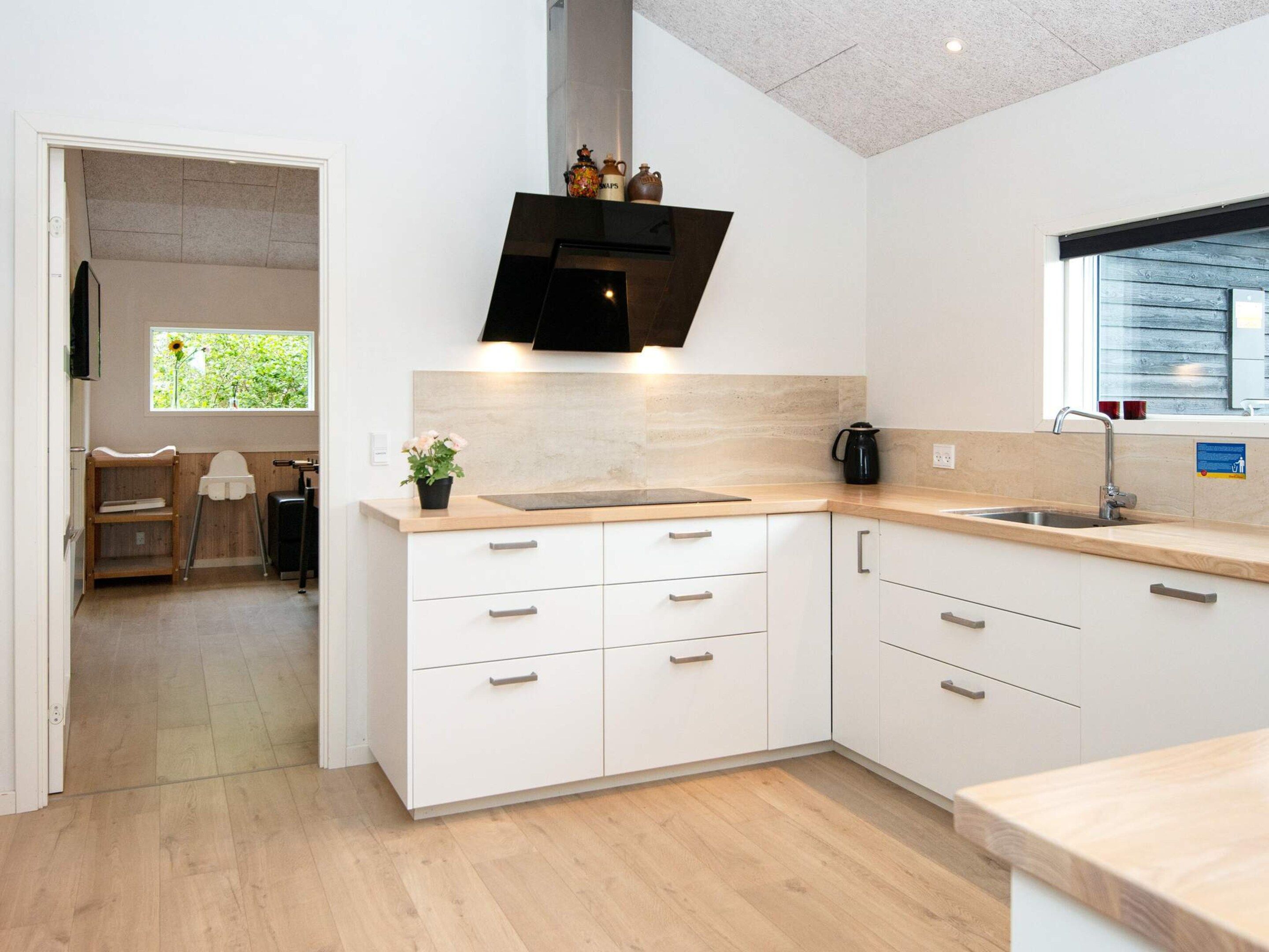 A modern kitchen with white cabinetry, a black range hood, and a window with a view of greenery.