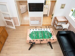 A living room with a foosball table, a black leather sofa, and a television mounted on the wall.