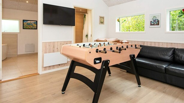 A room with a foosball table, a black leather sofa, and a television mounted on the wall.
