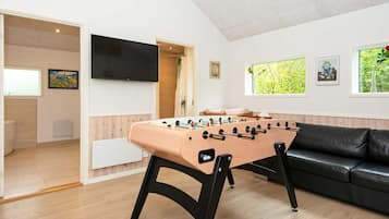 Quarto com mesa de pebolim, sofá de couro preto e televisão na parede.