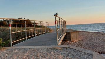 Un paseo marítimo que llega al mar, con barandilla metálica y un muro de hormigón.