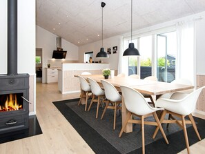 A modern kitchen with a central island, dining area with chairs, and a fireplace.
