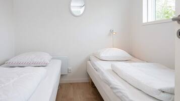 Un alojamiento pequeño, con una sola habitación, dos camas, una mesita de noche, un espejo en la pared y un ventanal que proporciona luz natural.
