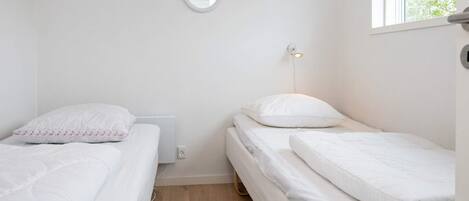 Un alojamiento pequeño, con una sola habitación, dos camas, una mesita de noche, un espejo en la pared y un ventanal que proporciona luz natural.