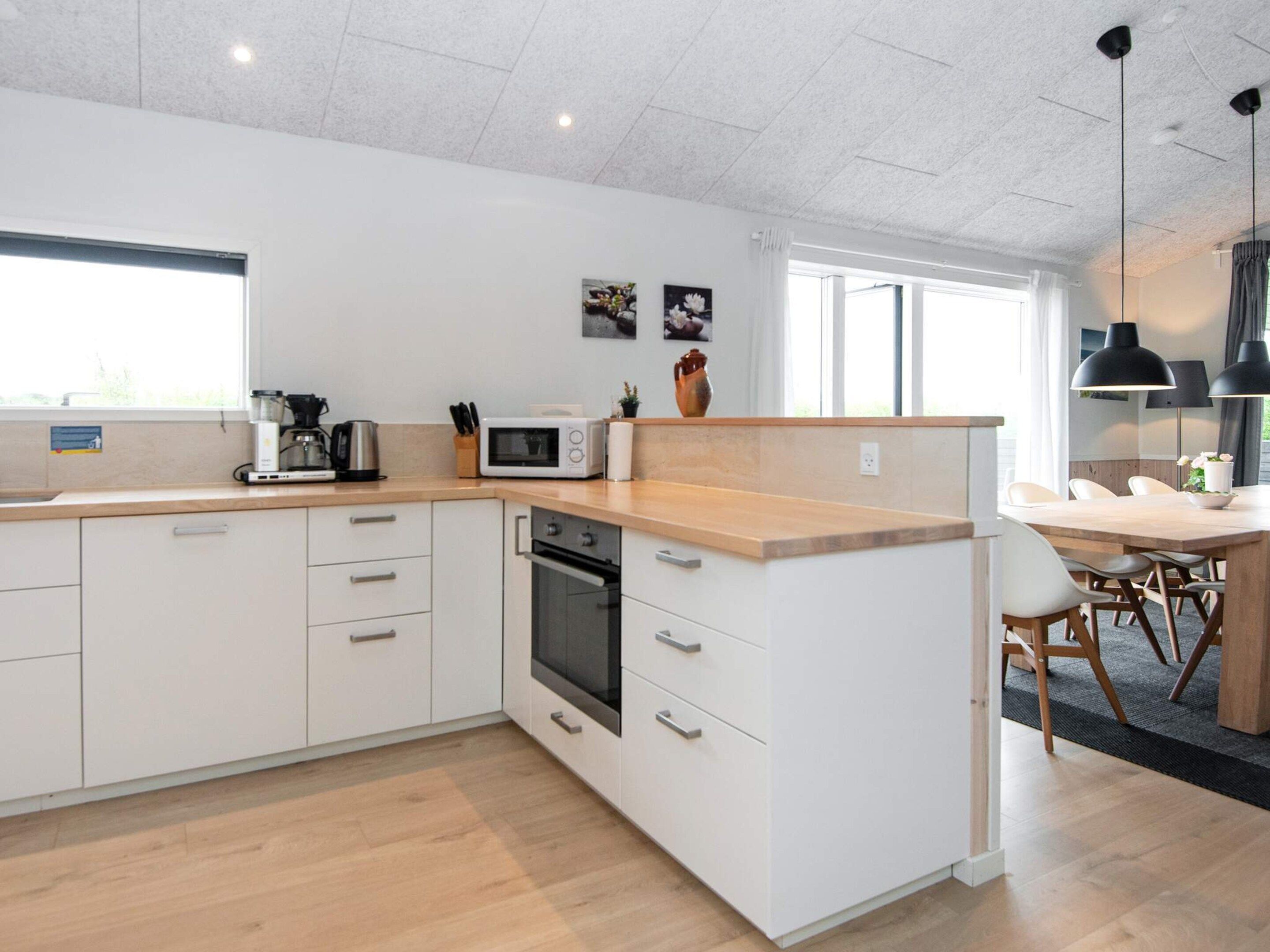 Una cocina moderna con armarios blancos, microondas y estufa. Hay un comedor con mesa y sillas.