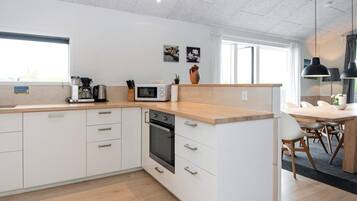 Una cocina moderna con armarios blancos, microondas y estufa. Hay un comedor con mesa y sillas.