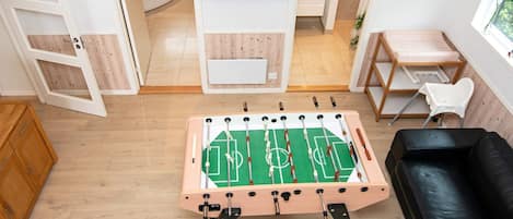 A room with a foosball table, a black leather sofa, and a TV mounted on the wall.