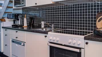 A kitchen with white cabinets, a black tiled backsplash, a microwave, a coffee maker, and a stove.