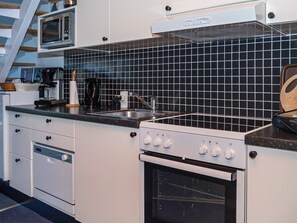 Una cocina con armarios blancos, salpicadero de baldosas negras, microondas, cafetera y estufa.