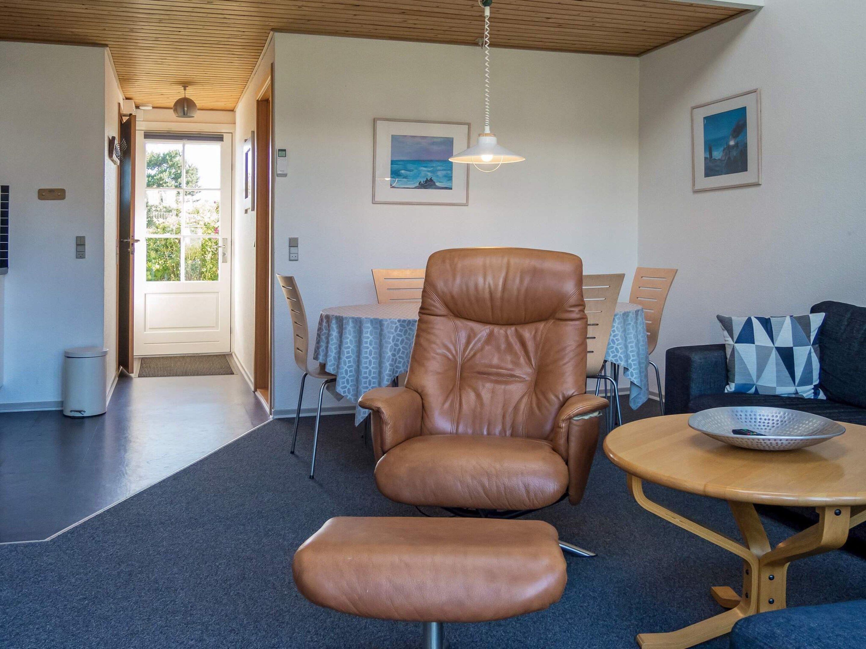 A room with a leather armchair, a wooden table with a bowl, a sofa, and a dining table with chairs.
