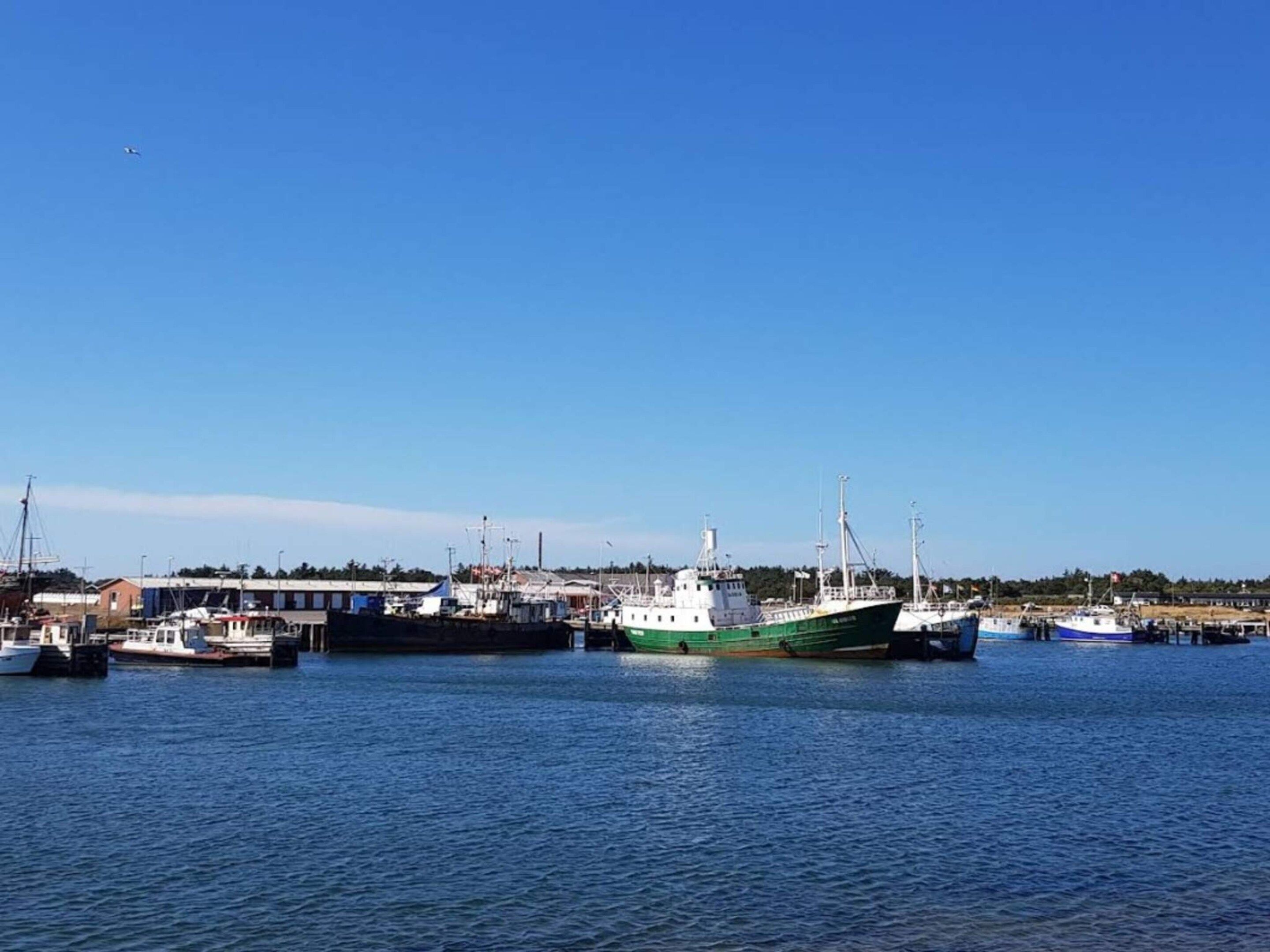 Un porto con diverse imbarcazioni ormeggiate, cielo sereno e mare calmo.