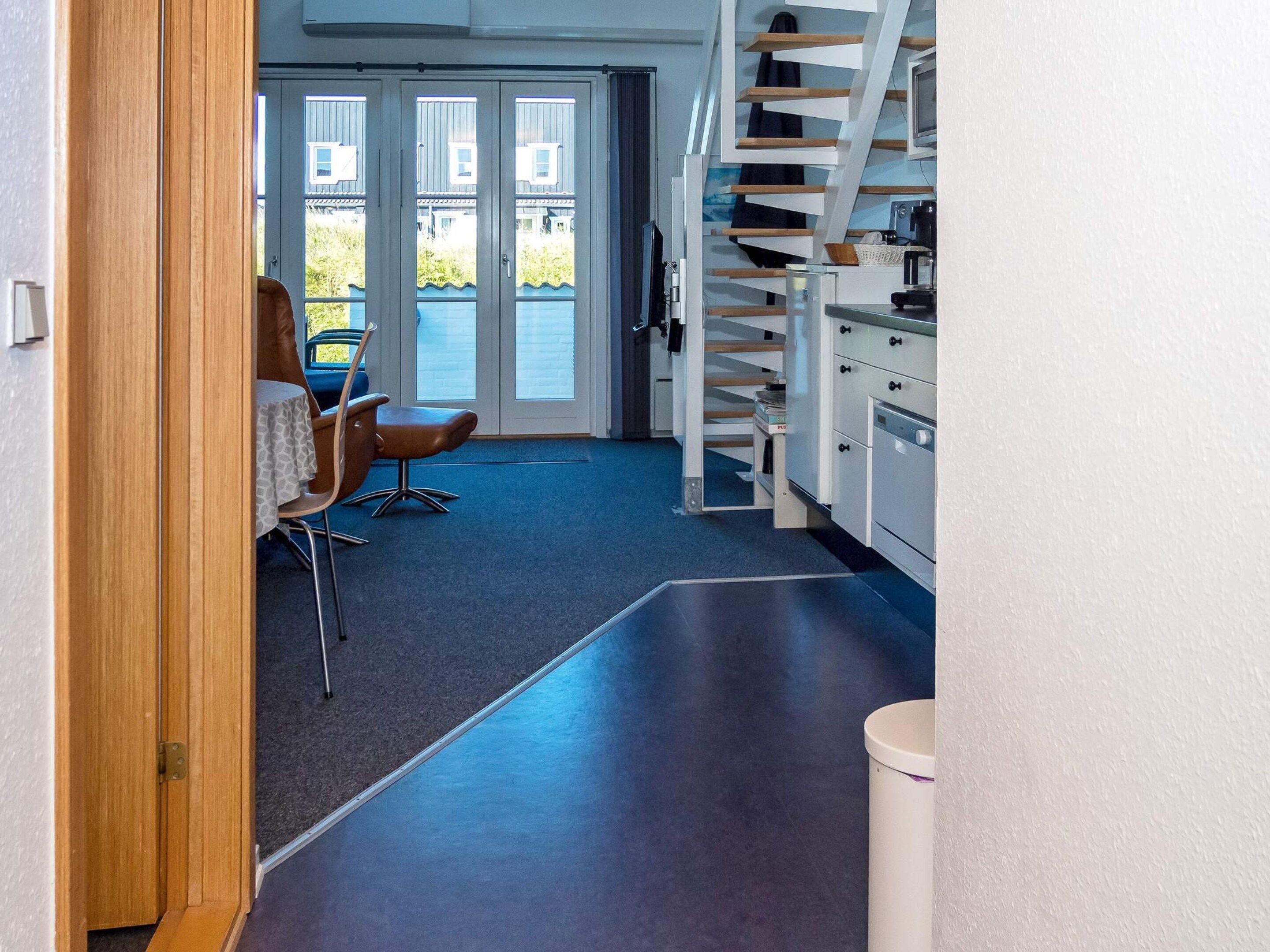 A narrow hallway with a dining area, a staircase, and a view of the outdoors.