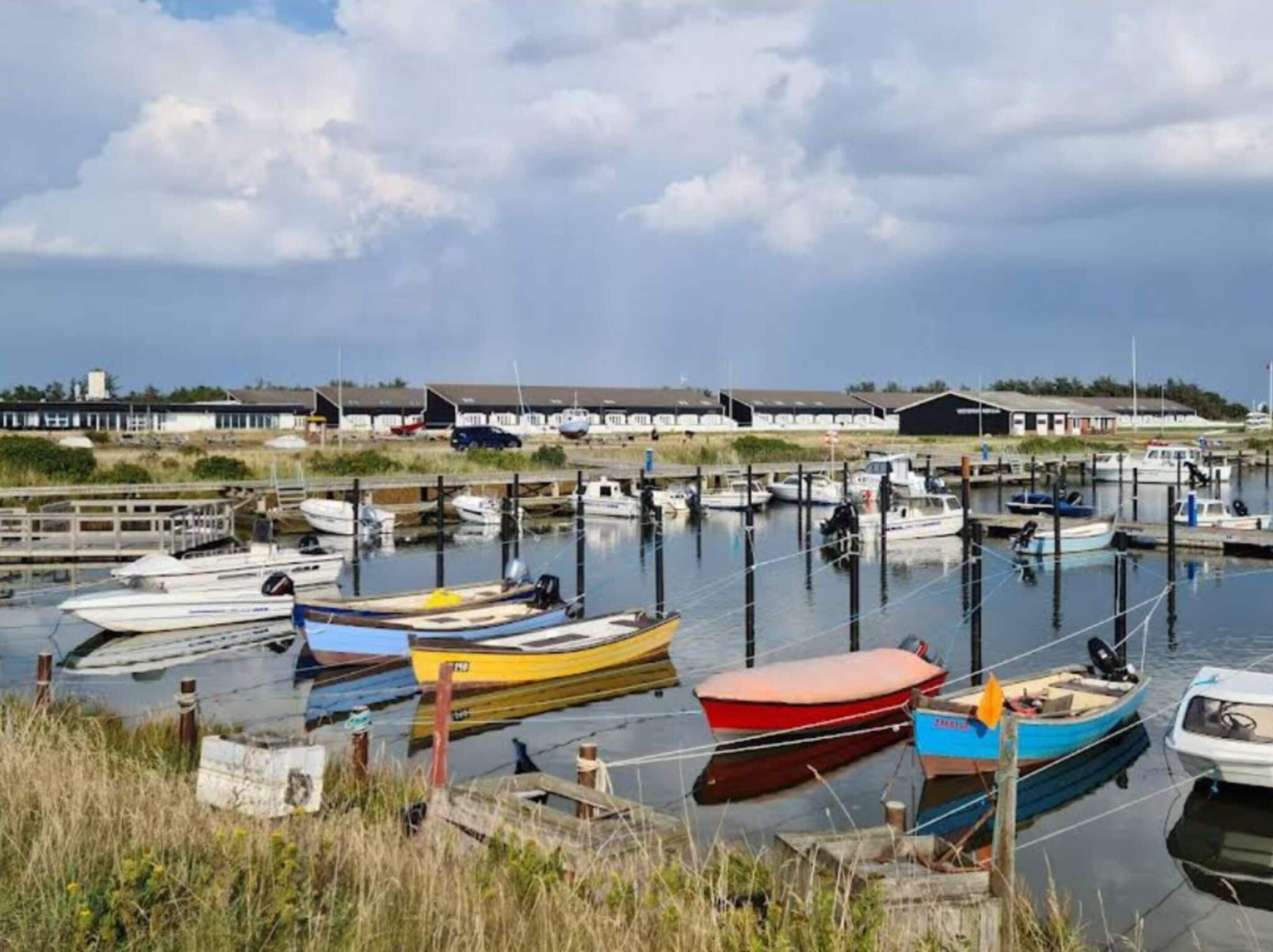 Un port de plaisance où sont amarrés différents types de bateaux, une jetée en bois et des bâtiments en arrière-plan.
