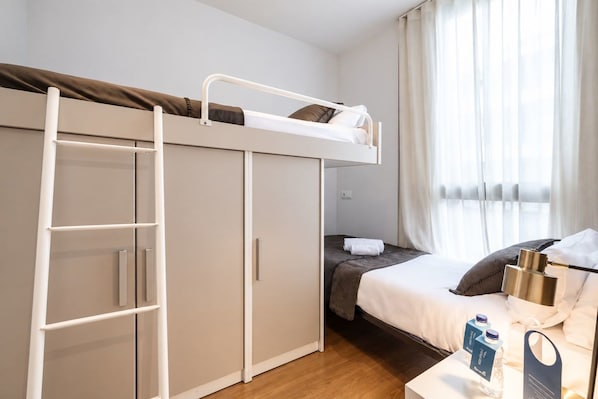 A bunk bed room with a ladder, a desk with a water bottle, and a bed with a pillow.