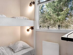Een slaapkamer met stapelbedden, een raam met uitzicht op bomen en een radiator.