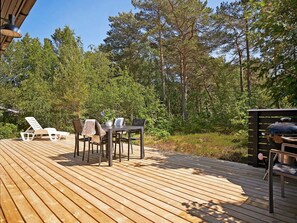 Une terrasse en bois, agrémentée de mobilier d’extérieur, entourée d’arbres.