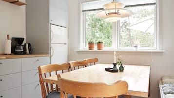 Una cocina con una mesa de comedor, sillas, cafetera y refrigerador.