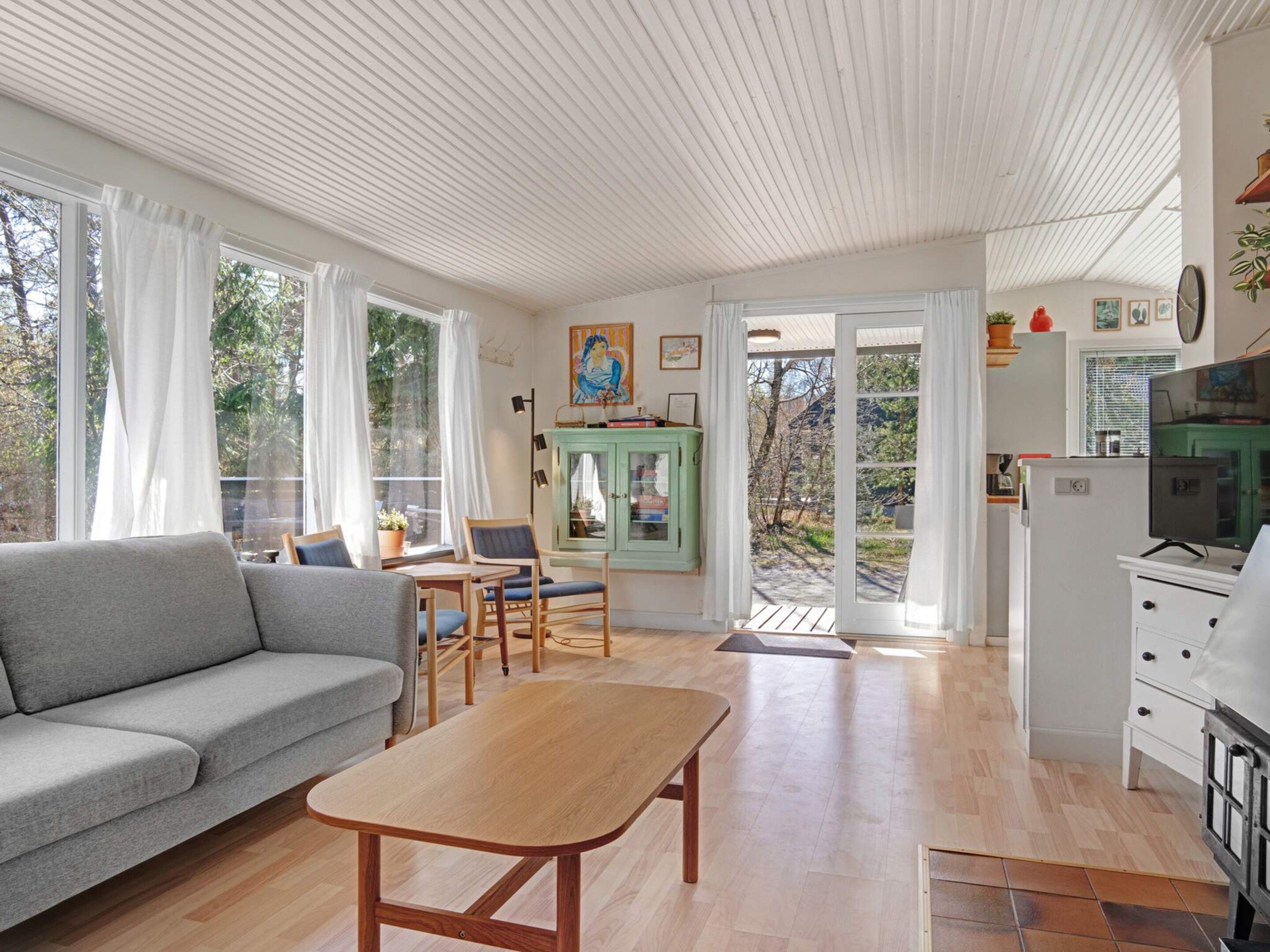 A modern living room with a sofa, a wooden table, and a kitchen area with a refrigerator and cabinets.
